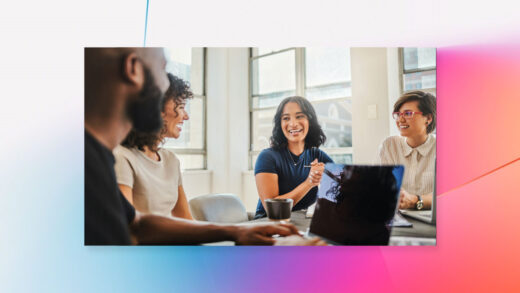 A diverse group of coworkers collaborate in an office space while one takes notes on his laptop.