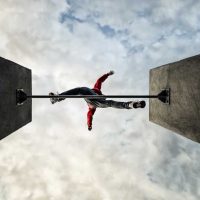 man jumps over obstacle, parkour leaps across gap, view from below looking up at cloud filled sky