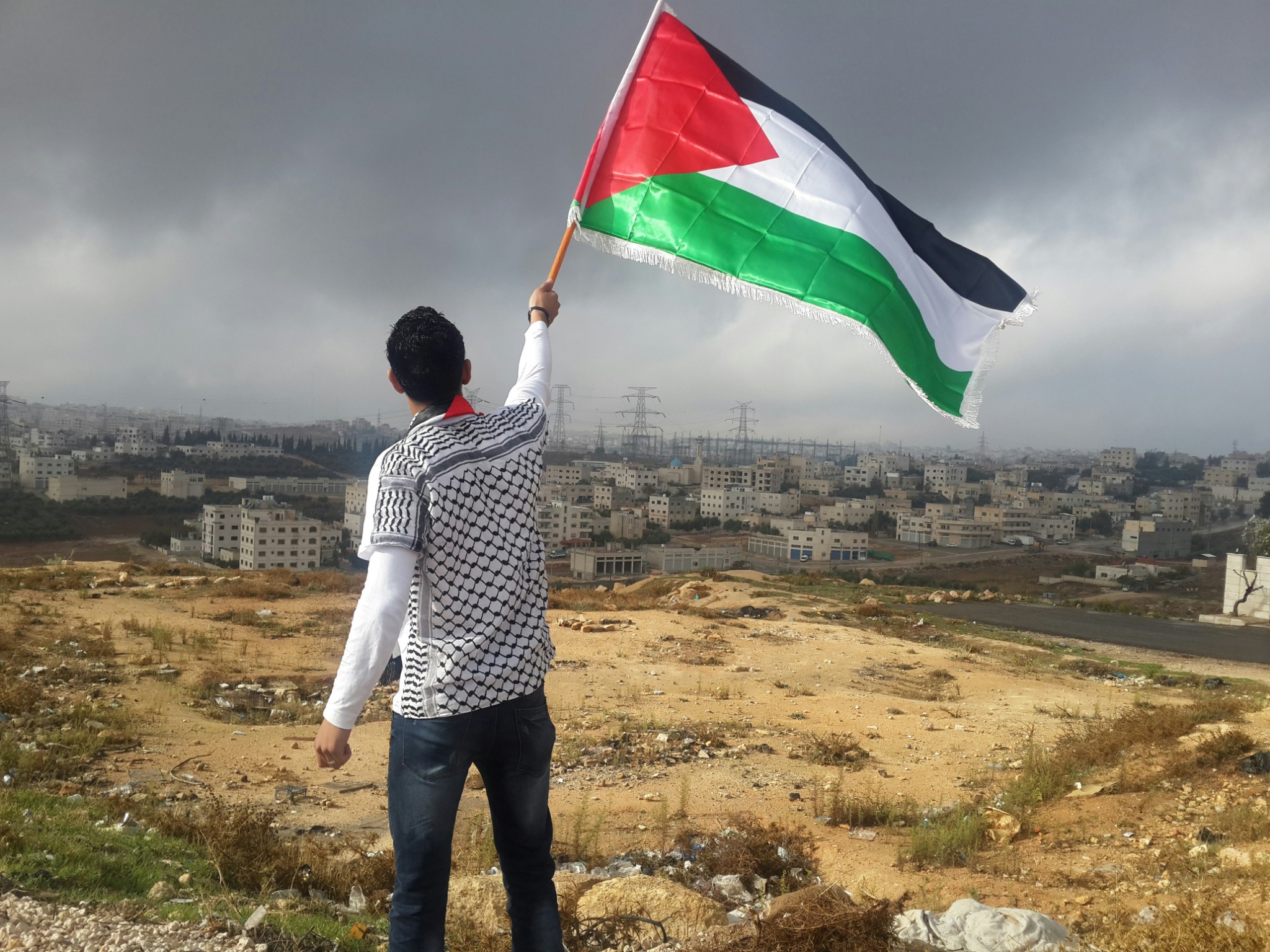 Man holding palestine flag over cityscape wallpaper