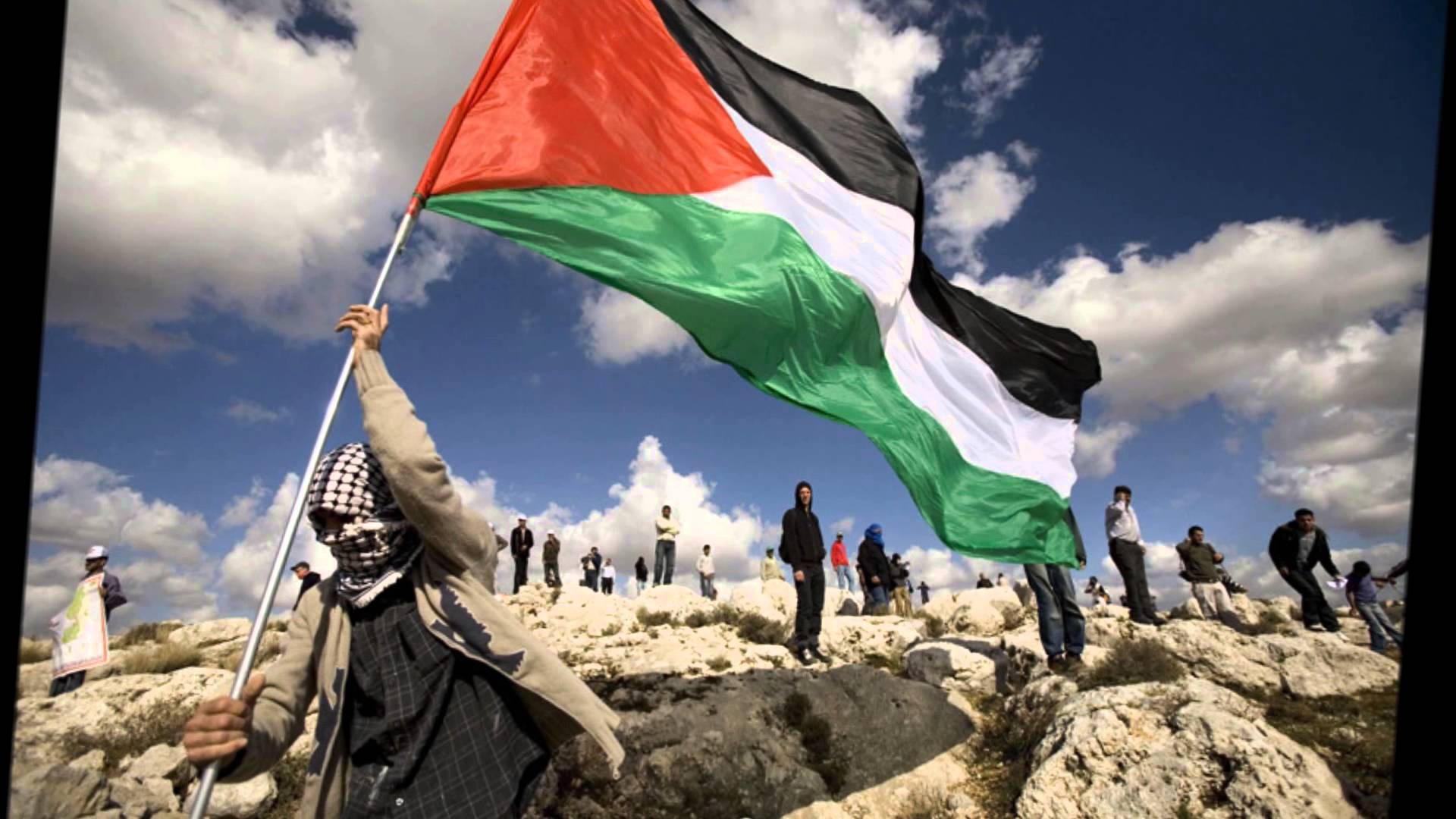 Palestinian flag held by masked figure on rocky terrain wallpaper