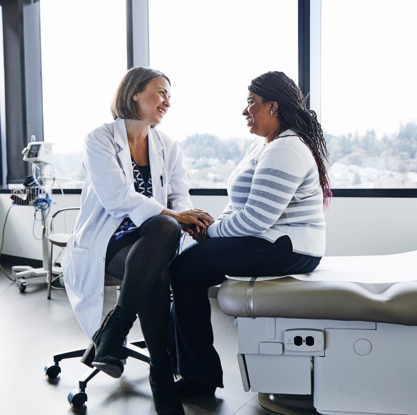 A smiling doctor talks with a woman in a hospital room.